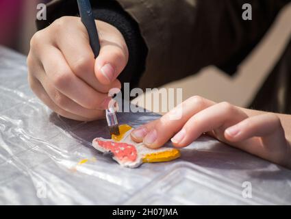 Nahaufnahme von Kinderhände Malerei Schmetterling Ton Dekoration mit Aquarellen Stockfoto