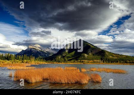 Die Kombination aus dramatisch stürmischem Himmel über dem Mount Rundle (2949 M) und wunderschönen warmen Sonnenuntergangslichtern auf den Vermilion Lakes im Vordergrund machen dieses Bild aus Stockfoto