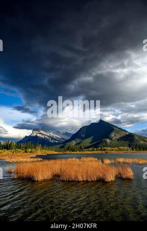 Die Kombination aus dramatisch stürmischem Himmel über dem Mount Rundle (2949 M) und wunderschönen warmen Sonnenuntergangslichtern auf den Vermilion Lakes im Vordergrund machen dieses Bild aus Stockfoto