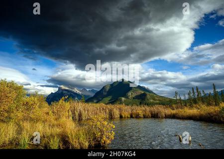 Die Kombination aus dramatisch stürmischem Himmel über dem Mount Rundle (2949 M) und wunderschönen warmen Sonnenuntergangslichtern auf den Vermilion Lakes im Vordergrund machen dieses Bild aus Stockfoto