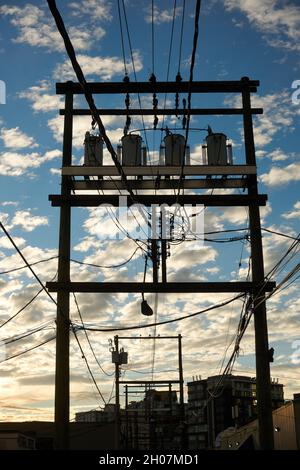 Reihe von elektrischen Verteilungstransformatoren, montiert auf einem H-Rahmen aus hölzernen Strommasten in der Dämmerung, im Hintergrund Altocumuluswolken Stockfoto