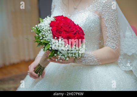 Hochzeitsstrauß in roter Rose. Brautpaar hält Hände.Braut und Bräutigam Hände mit Hochzeitsblumen. Zarte schöne Hochzeit Bouquet von rot Stockfoto