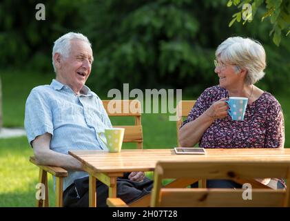 Seniorenpaar sitzt am Holztisch im Garten und trinkt Tee Stockfoto