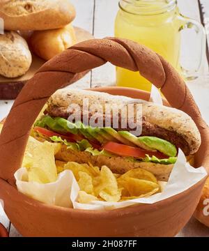 Tonkorb mit veganem Fleischsandwich mit Avocado, Tomaten und Salat, serviert mit Kartoffelchips Stockfoto