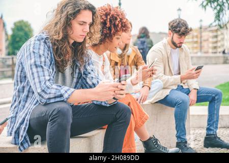 Multikulturelle Gruppe von Freunden mit Mobiltelefonen - Studenten sitzen in einer Reihe und tippen auf Smartphones Stockfoto