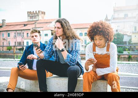 Multikulturelle Gruppe von Freunden mit Mobiltelefonen - Studenten sitzen in einer Reihe und tippen auf Smartphones Stockfoto