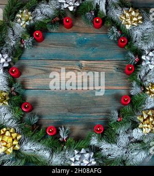 Ansicht von oben eines schneebedeckten Kranzes mit roten brennenden Kerzen und Bögen im Kreis Rand auf blau gealterten Holzplanken für die Winterferiensaison Stockfoto