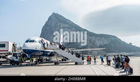 Passagiere (maskiert), die Schlange stehen, um einen Airbus A320-232 von British Airways zu besteigen, der auf dem Vorfeld des Flughafens von Gibraltar geparkt ist. Stockfoto