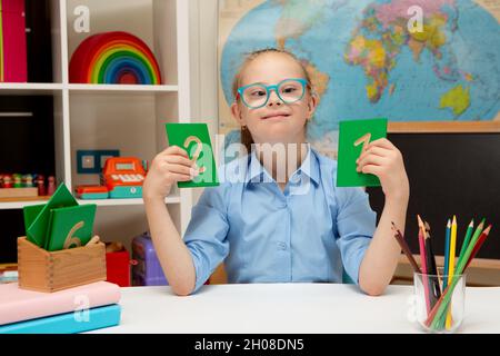 Ein schönes Mädchen mit Down-Syndrom ist in der Klasse beschäftigt und studiert Zahlen Stockfoto