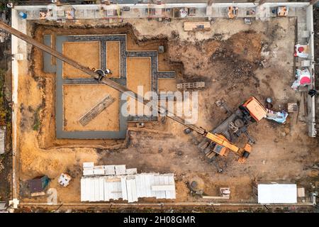 Gründung eines zukünftigen Hauses. Gießfundament mit Zement auf Baustelle mit Kran, Luftaufnahme. Stockfoto