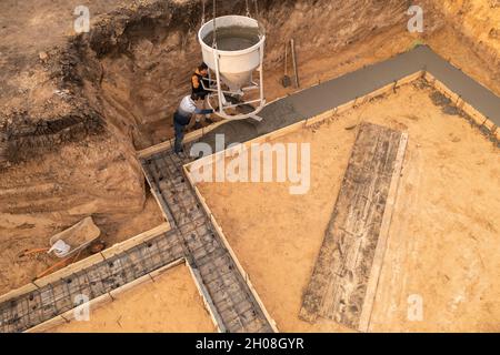 Baustelle mit Arbeitskräften, die Beton in Schalung mit Bewehrung gießen. Feuchter Zement fließt in das Fundament des zivilen Gebäudes, Luftaufnahme. Stockfoto