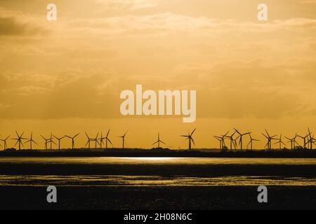 Norderney, Deutschland. Oktober 2021. Ein Windpark ist an der ostfriesischen Nordseeküste vor Norderney gegen die aufgehende Sonne gesehen, die einen dramatischen Himmel erzeugt. Quelle: Matthias Oesterle/Alamy Live News Stockfoto