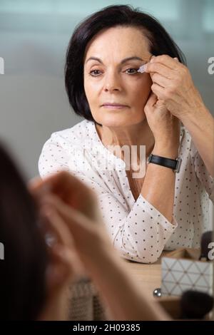 Gut aussehende ältere Frau, die vor dem Spiegel schminke Stockfoto