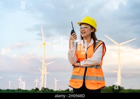 Junge Ingenieurin mit Walkie Talkie, um das System gegen zu überprüfen Windturbinenpark Stockfoto