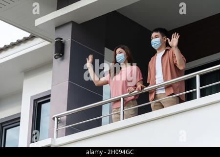 Quarantänepaar trägt eine Gesichtsmaske und begrüßt Nachbarn vom Balkon des Hauses, Coronavirus(covid-19) Pandemie Stockfoto