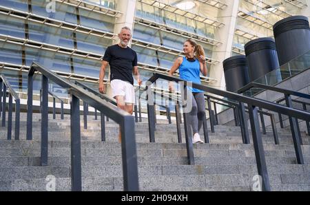 Fröhliches reifes Paar, Mann und Frau in Sportkleidung, die gemeinsam im Freien trainieren und auf der Treppe in der Stadt stehen Stockfoto