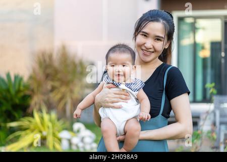 Glückliche Mutter hält neugeborenes Baby in einer zarten Umarmung vor ihrem Haus Stockfoto