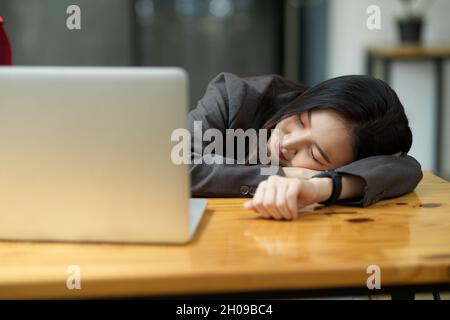 Müde oder erschöpfte junge Geschäftsfrau, die im Büro vor ihrem Laptop am Schreibtisch schlappte Stockfoto