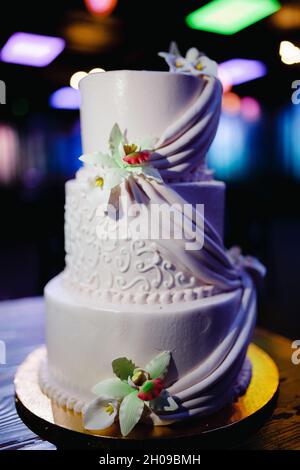 Hochzeitslocation: Grüner und violetter Restaurantsaal mit Neonbeleuchtung und weißem dreistufigem Kuchen. Stockfoto
