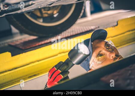 Thema Automobilindustrie. Kaukasischer Automechaniker mit Taschenlampe in der Hand Durchführen von Fahrzeug-Suspension-Check. Stockfoto