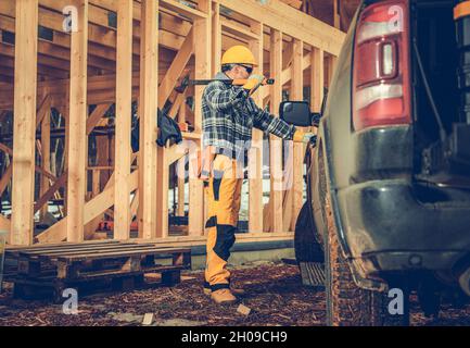 Kaukasischer Auftragnehmer mit großem Hammer vor dem neu errichteten Holz-Skelett-Haus Stockfoto