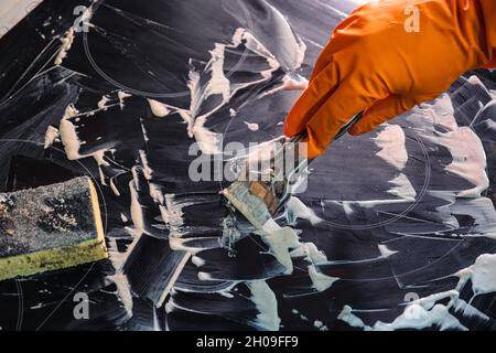 Orangefarbener Handschuh, Metallschaber, Schwamm und Schaumreiniger. Waschen des Kochfelds. Selektiver Fokus. Das Konzept der Hausreinigung eines Elektroofens Stockfoto