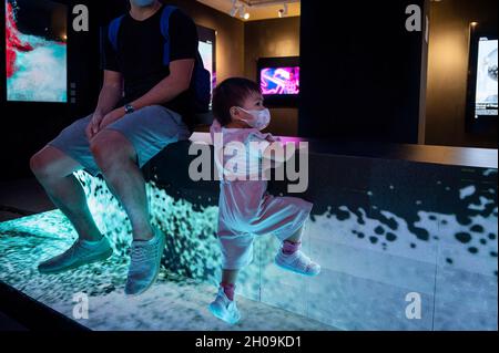 Hongkong, China. Okt. 2021. Ein junger Besucher klettert auf der Digital Art Fair Asia in Hongkong, China, am 08. Oktober 2021 ein Kunstwerk der Tech-Installation des Multimedia-Künstlers Victor Wong. Die Messe zeigt NFT Crypto Art, nicht-fungible Token, als Teil des neuen Trends in der modernen Kunst. (Bild: © Miguel Candela/SOPA Images via ZUMA Press Wire) Stockfoto