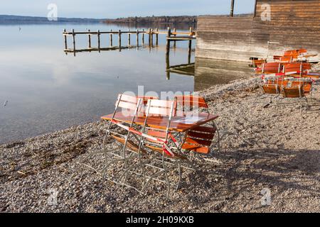 Herrsching, Deutschland - 4. Feb 2021: Biergartentisch und -Stühle mit Sperrband verschlossen. Ammersee im Hintergrund. Während der Covid-19-Sperre. Stockfoto