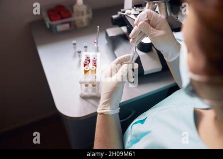 Weibliche Labortechnikerin nimmt mit moderner Ausrüstung Proben vom Reagenzglas zum Forschungsmaterial am Arbeitsplatz Stockfoto