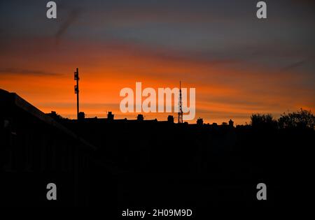 Brighton UK 12. Oktober 2021 - Ein wunderschöner Sonnenaufgang über den Dächern von Brighton und der Whitehawk Hill Sendestation, während der trockene warme Zauber des Wetters im Südosten andauert : Credit Simon Dack / Alamy Live News Stockfoto