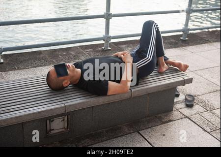 '11.07.2019, Singapore, , Singapur - Ein Mann liegt auf einer Bank am Ufer des Singapore River und bedeckt seine Augen mit einem Geldbeutel. 0SL190711D001CAROEX.JPG Stockfoto