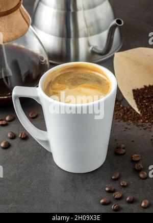 Eine Tasse Kaffee und die dritte Generation gießen über die Kaffeemaschine auf dem Steinboden Stockfoto