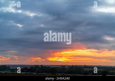 Sonnenaufgang versteckt hinter dicken zerbrochenen Wolken, Stratocumulus, über der Kent Landschaft im Herbst. Niedriger Horizont mit etwas orangefarbenem und gelbem Himmel und Wolken mit dunkelgrauen Wolken oben in einer fast festen Schicht. Stockfoto