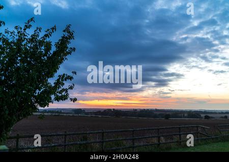 Sonnenaufgang versteckt hinter dicken zerbrochenen Wolken, Stratocumulus, über der Kent Landschaft im Herbst. Niedriger Horizont mit etwas orangefarbenem und gelbem Himmel und Wolken mit dunkelgrauen Wolken oben in einer fast festen Schicht. Stockfoto