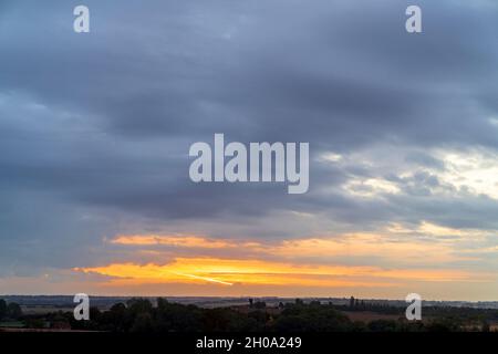 Sonnenaufgang versteckt hinter dicken zerbrochenen Wolken, Stratocumulus, über der Kent Landschaft im Herbst. Niedriger Horizont mit etwas orangefarbenem und gelbem Himmel und Wolken mit dunkelgrauen Wolken oben in einer fast festen Schicht. Stockfoto