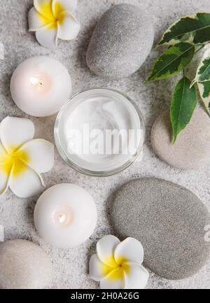 Spa-Behandlung mit Massagesteinen und feuchtigkeitsspendender Creme auf grauem Betongrund Stockfoto