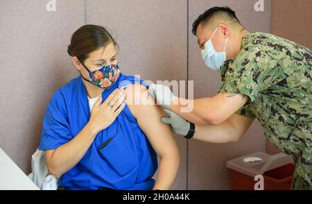 AGANA HEIGHTS, Guam (Jan 4, 2021) – Hospital Corpsman 2. Klasse Mark Forrey, dem U.S. Naval Hospital Guam (USNH Guam) zugeordnet, desinfiziert den Arm von LT. Cmdr. Allison Wessner, eine Kinderärztin, die dem USNH Guam zugewiesen wurde, bevor sie einen COVID-19-Impfstoff verabreichte. Das US-Verteidigungsministerium hat bei seiner ersten Lieferung eine begrenzte Menge an COVID-19-Impfdosen erhalten und verabreicht den Impfstoff derzeit an Mitarbeiter der Phase 1a, darunter Gesundheitsdienstleister und Support-Mitarbeiter, Rettungsdienste und Mitarbeiter der öffentlichen Sicherheit. Stockfoto