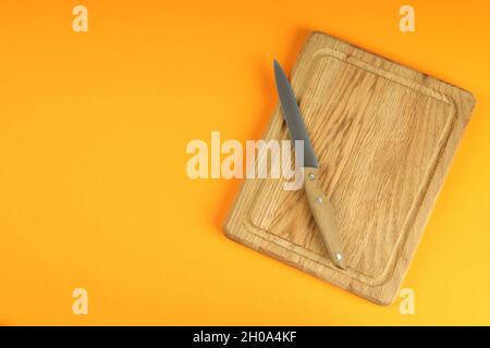Schneidebrett mit Messer auf orangefarbenem Hintergrund. Stockfoto