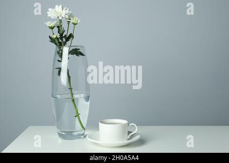 Vase mit Chrysanthemen und Tasse Kaffee auf weißem Tisch. Stockfoto