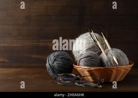Mehrfarbige Garnkugeln mit Stricknadeln in einem Korbkorb auf einem Holzhintergrund. Stockfoto