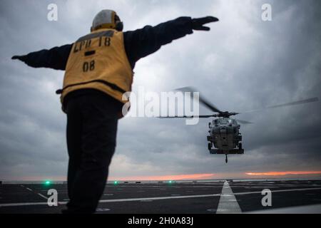 PHILIPPINISCHES MEER (Jan 6, 2021) Aviation Boatswain's Mate (Handling) Airman Chase Bice aus Houston leitet die Landung eines MH-60S-Hubschraubers, der dem Hubschrauber Sea Combat Squadron (HSC) 12 auf dem Flugdeck des amphibischen Transportschiffes USS New Orleans (LPD 18) zugewiesen wurde. New Orleans, Teil der America Amphibious Ready Group, arbeitet zusammen mit der 31. Marine Expeditionary Unit im Verantwortungsbereich der 7. US-Flotte, um die Interoperabilität mit Verbündeten und Partnern zu verbessern und als einsatzbereite Einsatztruppe zur Verteidigung von Frieden und Stabilität in der Indo-Pazifik-Region zu dienen. Stockfoto