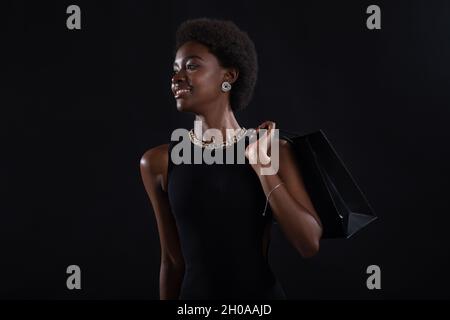 afroamerikanische Frau mit Afro-Frisur hält schwarze Einkaufstaschen. Verkauf und Rabatte auf den Markt Going Black Friday Konzept. Stockfoto