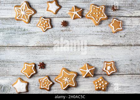 Rand von weihnachtlichen Lebkuchen in Sternform mit Glasur- und Gewürzmustern auf weißem Holzhintergrund. Draufsicht mit Kopierbereich Stockfoto