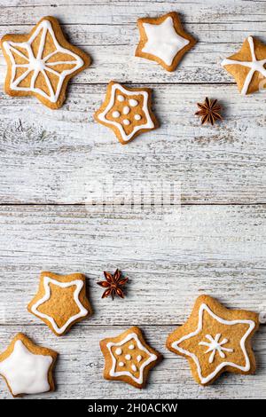Rand von weihnachtlichen Lebkuchen in Sternform mit Glasur- und Gewürzmustern auf weißem Holzhintergrund. Draufsicht mit Kopierbereich Stockfoto