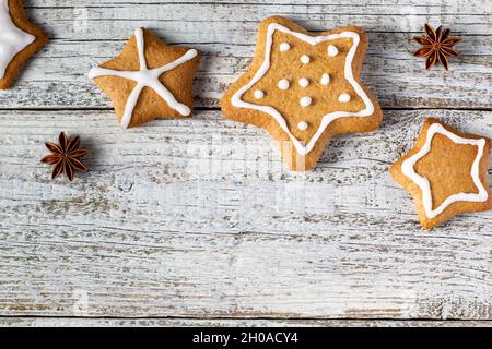 Rand von weihnachtlichen Lebkuchen in Sternform mit Glasur- und Gewürzmustern auf weißem Holzhintergrund. Draufsicht mit Kopierbereich Stockfoto