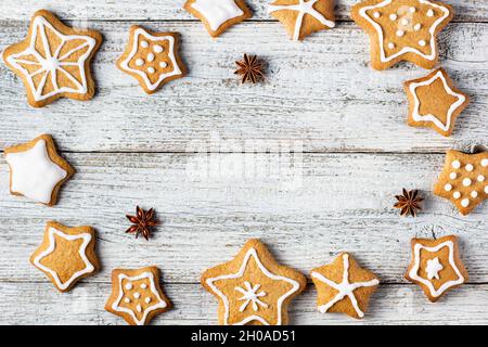 Rahmen aus weihnachtlichen Lebkuchen in Sternform mit Glasur- und Gewürzmustern auf weißem Holzhintergrund. Draufsicht mit Kopierbereich Stockfoto