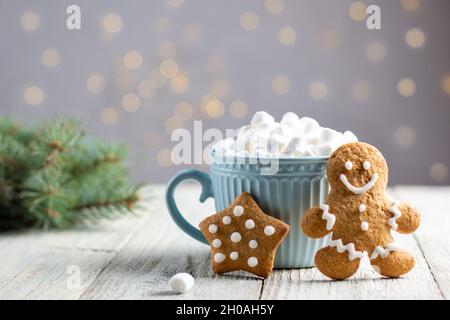 Eine blaue Tasse warmes Getränk mit Marschwalben und Lebkuchen auf weißem Holzhintergrund. Festliche Weihnachten Hintergrund. Traditionelle Weihnachten Stockfoto