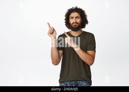 Unzufriedener Mann aus der Mitte des ostermondes, der mit skeptischem Grimasse mit den Fingern auf die obere linke Ecke zeigt, mag das nicht, er steht auf weißem Hintergrund Stockfoto