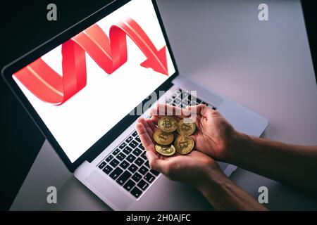 Draufsicht auf die Hände mit Bitcoins. Auf dem Computerbildschirm zeigt der rote Pfeil nach unten. Stockfoto