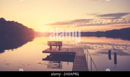 Schöner Sonnenuntergang über dem See mit Holzbank am Pier. Stockfoto